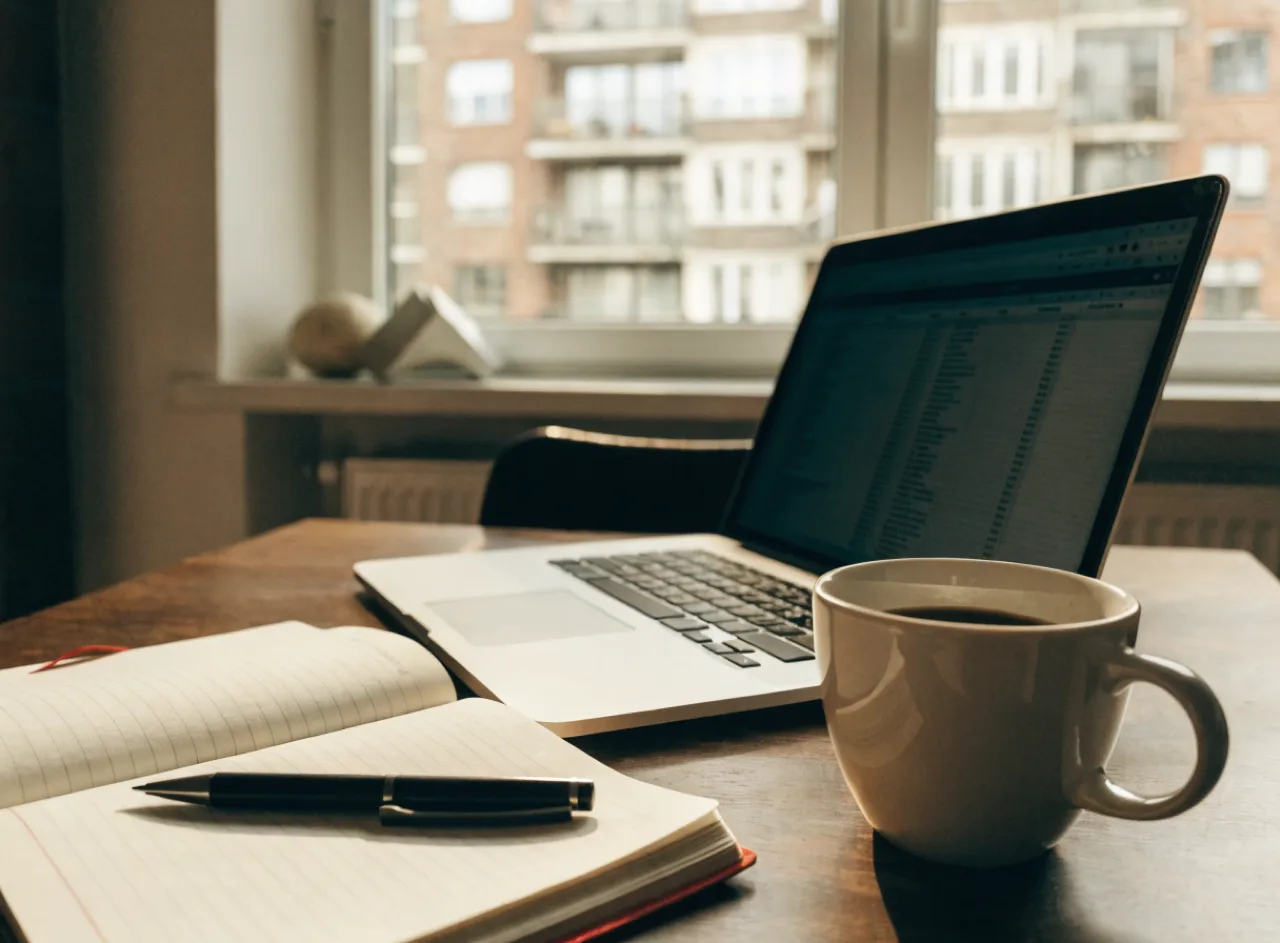 Desk with a laptop open to a video call, lit by a window at dusk.